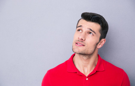 Thoughtful casual man looking up at copyspace over gray backgroundの写真素材