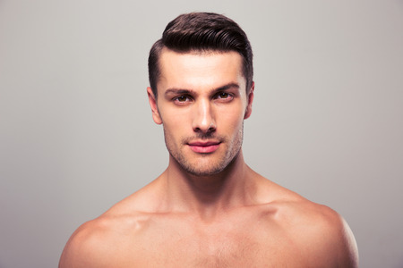 Handsome young man with nude torso looking at camera over gray backgroundの写真素材