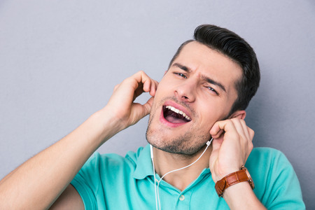 Young man singing in headphones over gray background