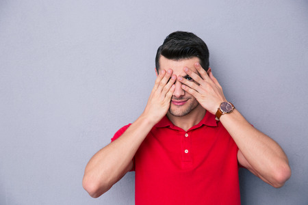 Casual man covering his eyes with fingers over gray backgroundの写真素材