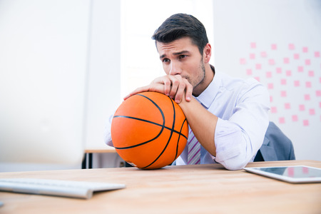Pensive businessman sitting at the table with ball in office. Looking awayの写真素材