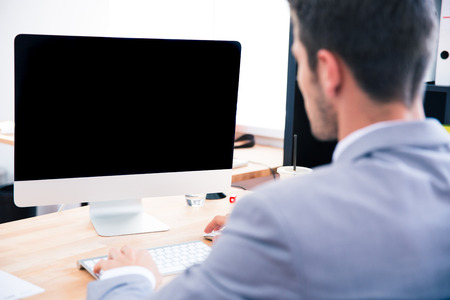 Back view portrait of a businessman sitting at the table with blank monitorの写真素材