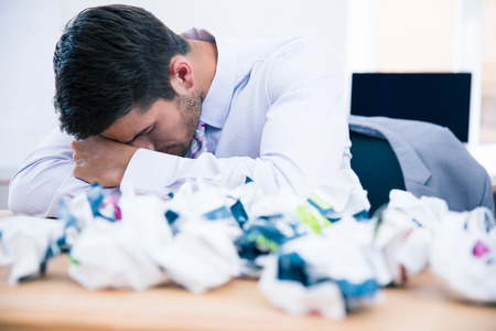 Tired businessman sitting at the table with crumpled of paper in officeの写真素材