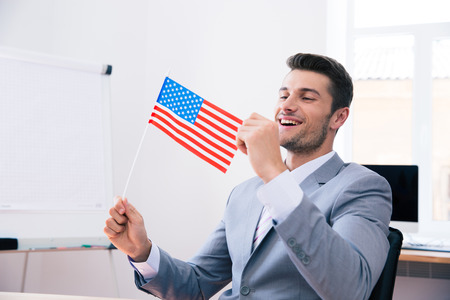 Cheerful handsome businessman holding USA flag in officeの写真素材