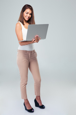 Full length portrait of a happy businesswoman using laptop over gray backgroundの写真素材
