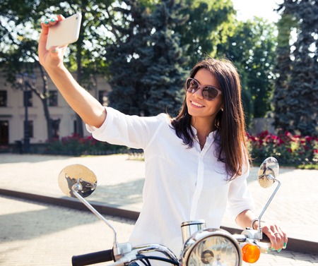 Happy young woman on scooter making selfie photo on smartphoneの写真素材