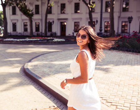 Happy woman in sunglasses and dress walking outdoors. Looking at camera