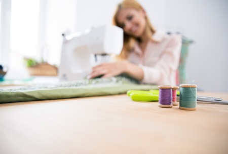 Female designer sitting at teh table and working on sewing machine. Focus on equipmentの写真素材