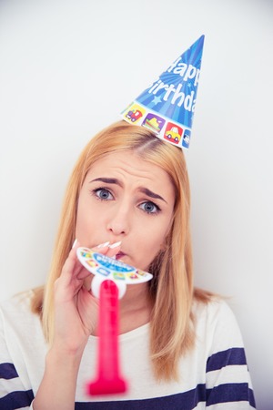 Young girl with party hat and blows whistle over gray background. Looking at cameraの写真素材