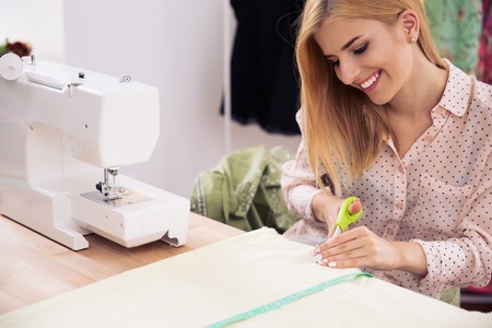 Happy female designer cutting cloth in workshop