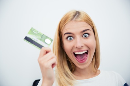 Cheerful young woman holding bank card over gray backgroundの写真素材