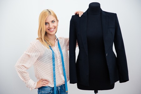 Smiling fashion designer standing near mannequin over gray background. Looking at camera