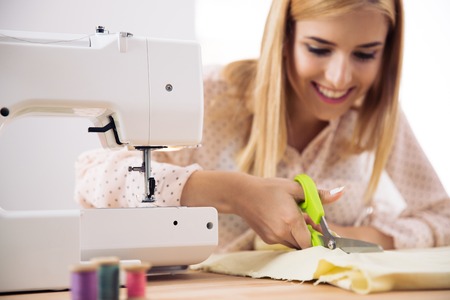 Smiling female designer cutting cloth in workshopの写真素材