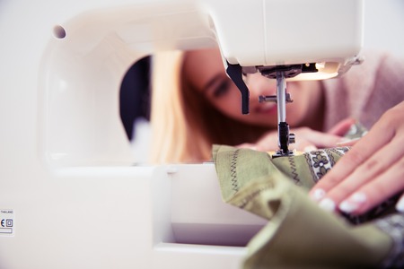 Closeup portrait of female designer using sewing machine in workshop. Focus on machineの写真素材