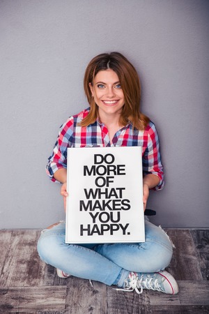 Smiling woman sitting on the floor and holding board with motivational phraseの写真素材