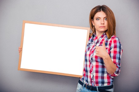 Young casual woman holding blank board and showing thumb up over gray backgroundの写真素材