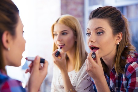 Two young girls looking at mirror and applying lipstickの写真素材