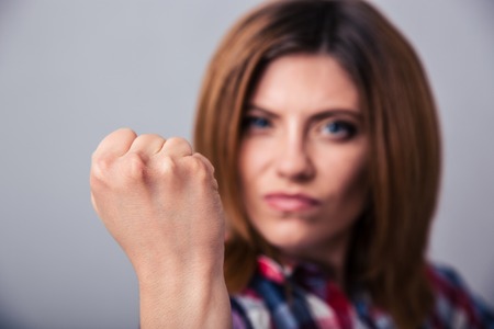 Angry young woman showing fist over gray background. Focus on fistの写真素材