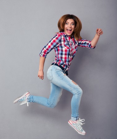 Funny young woman jumping over gray background and looking at cameraの写真素材