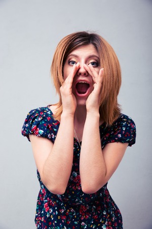 Young woman shouting with palms at camera over gray backgroundの写真素材