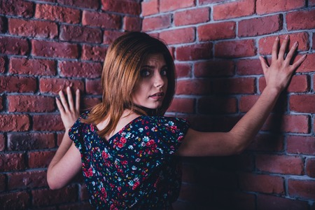 Scared young woman standing in corner of brick wall and looking at cameraの写真素材
