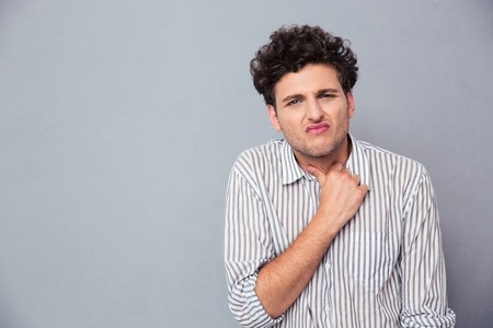 Casual man with curly hair having neck ache over gray backgroundの写真素材