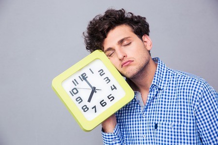 Tired man holding big clock over gray backgroundの写真素材