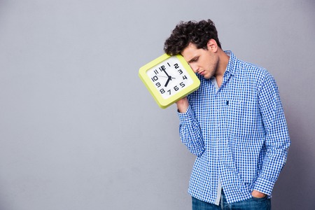 Tired man holding big clock over gray backgroundの写真素材