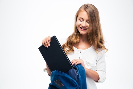Happy young woman putting book into backpack isolated on a white background