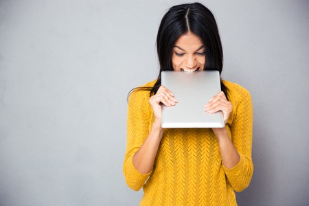 Angry woman biting tablet computer over gray background