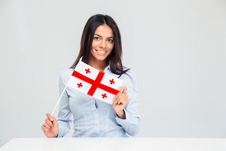 Smiling young woman sitting at the table with georgian flag isolated on a white background. Looking at cameraの写真素材