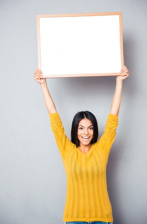 Portrait of a smiling woman holding blank board over gray backgroundの写真素材