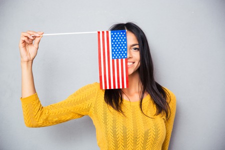 Happy young woman covering her face with american flag over gray background