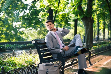 Thoughtful businessman sitting on the bench with tablet computer and looking awayの写真素材