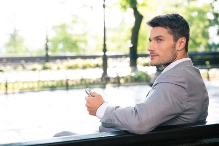 Thoughtful businessman sitting on the bench with tablet computer outdoors and looking awayの写真素材