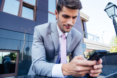 Handsome businessman using smartphone outdoors near office buildingの写真素材