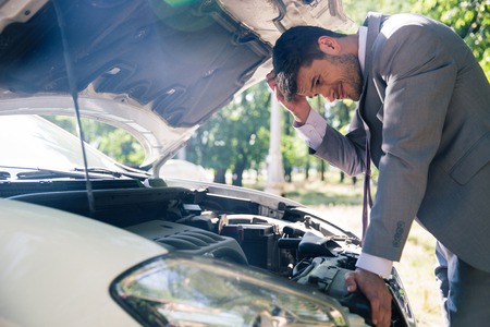 Man in suit looking under the hood of breakdown car outdoors