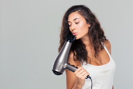 Portrait of a young pretty woman blowing on hairdryer over gray backgroundの写真素材