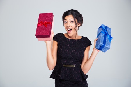 Laughing woman in black dress holding two gift boxes on gray background. Looking at camera