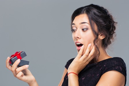 Portrait of amazed woman holding gift box on gray backgroundの写真素材