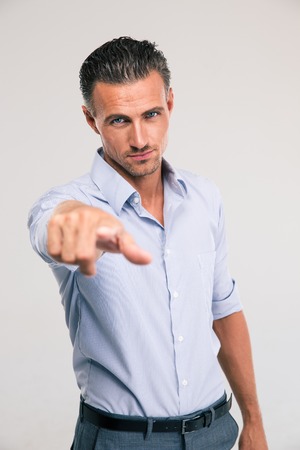 Portrait of a handsome businessman pointing finger at camera over gray background
