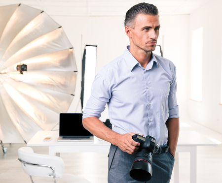 Portrait of a handsome photographer standing with camera in studioの写真素材