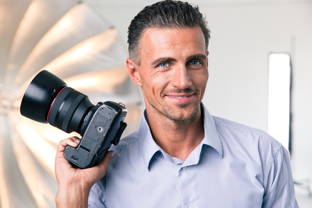 Portrait of a happy photographer holding camera in studioの写真素材
