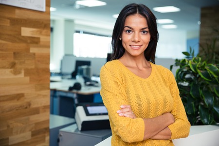 Portrait of a smiling businesswoman standing with arms folded in office and looking at cameraの写真素材