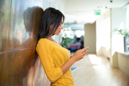 Side view portrait of a businesswoman in sweater using smartphone in hallway