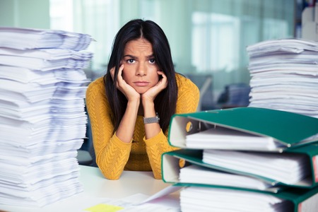 Portrait of a tired casual businesswoman sitting at the table in office and looking at camera