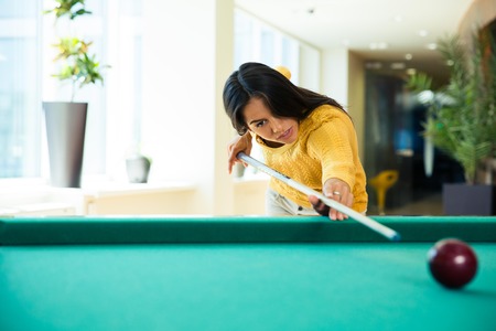 Beautiful young woman playing billiards indoors