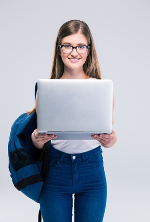 Portrait of a smiling female teenager standing with backpack and laptop isolated on a white backgroundの写真素材