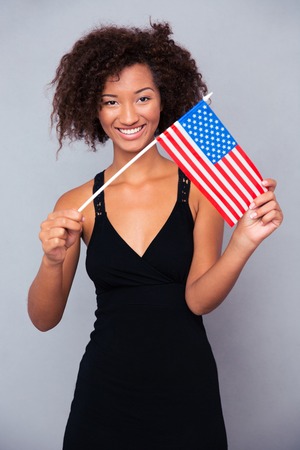 Portrait of a happy afro american woman holding USA flag over gray background and looking at cameraの写真素材