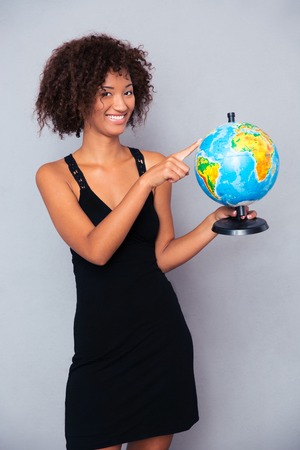 Portrait of a happy african woman holding globe over gray backgroundの写真素材